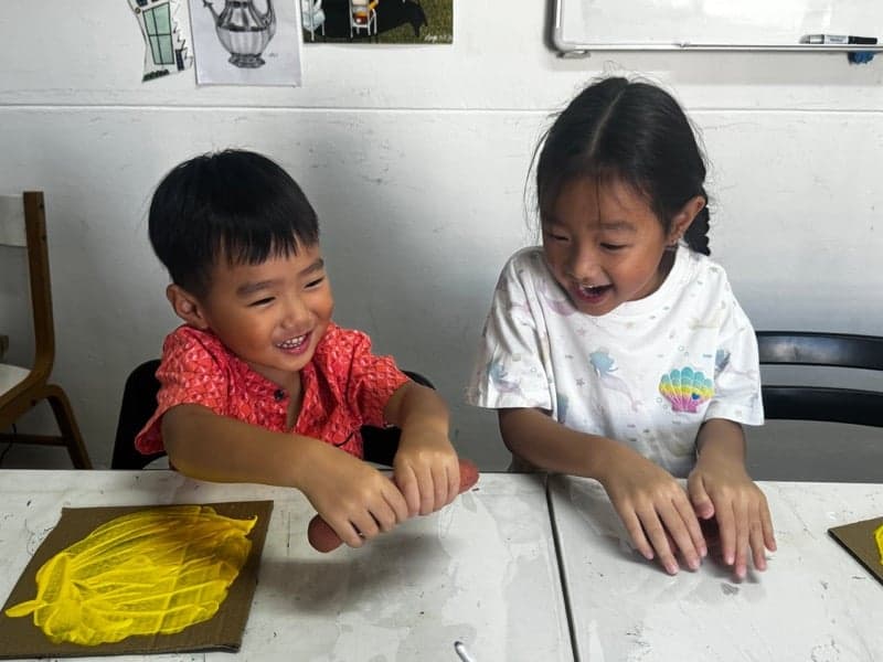 Two young children hand-printing with yellow paint at an Art by Ancourage Crafty Corner class in Singapore