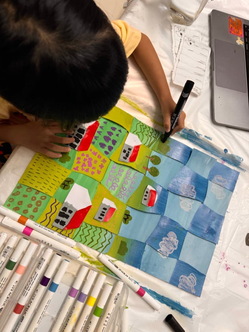 Student outlining a mixed-media patchwork landscape with marker over acrylic at Art by Ancourage