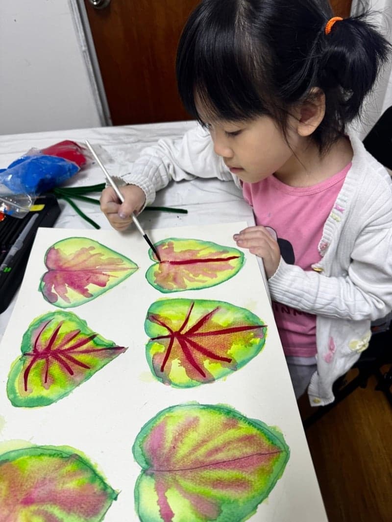 Young child painting a sheet of watercolour leaves in an Art by Ancourage Mini Masters class