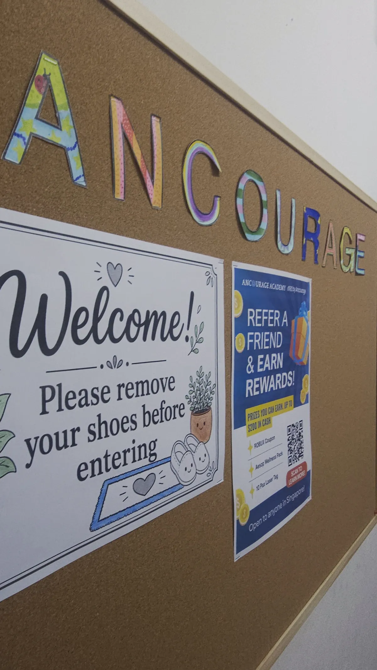 Welcome noticeboard at Ancourage Academy Bishan with hand-lettered 'Ancourage' signage and a remove-your-shoes notice.