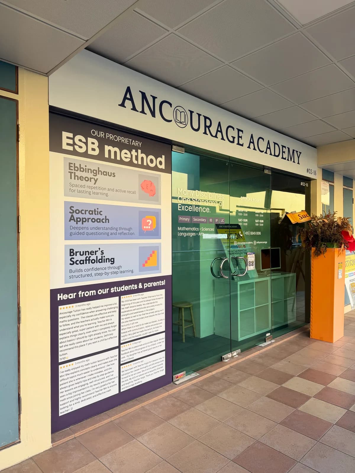 Ancourage Academy Woodlands shopfront at Vista Point #02-16 — fascia signage above the ESB method panel and the 'Hear from our students & parents' review wall.