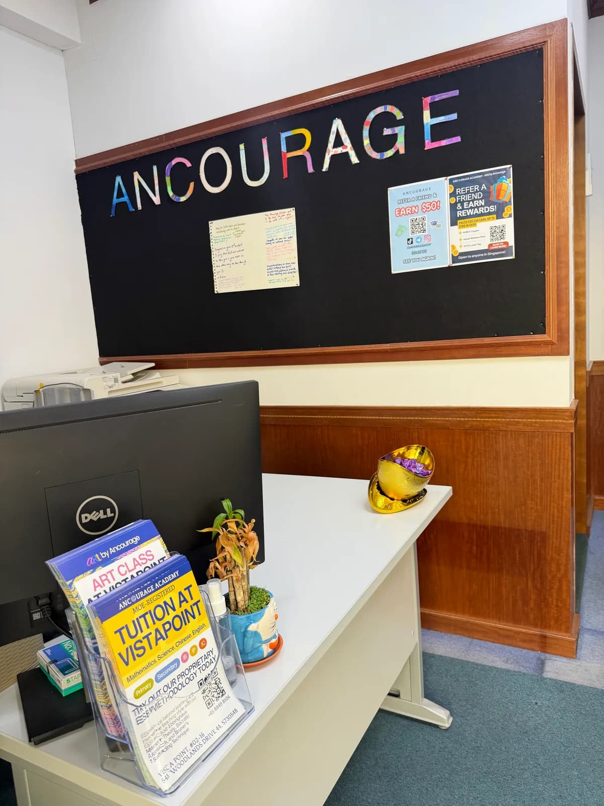Reception at Ancourage Academy Woodlands with the hand-lettered Ancourage noticeboard and 'Tuition at Vista Point' class guides on the counter.